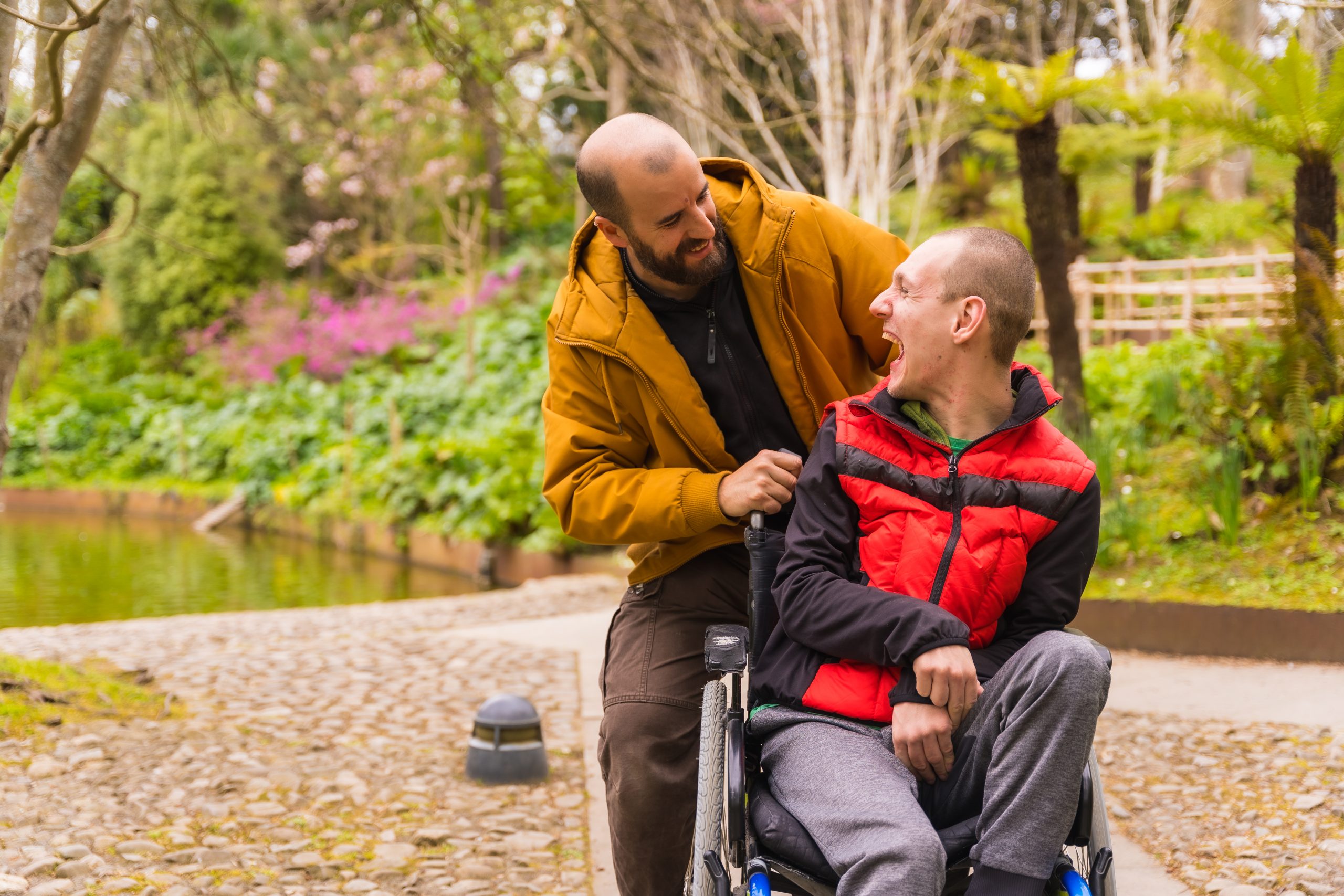 A disabled person in a public city park in the wheelchair, having fun walking with a friend